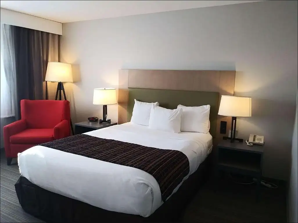A queen room with a red armchair beside the window and a bedside telephone