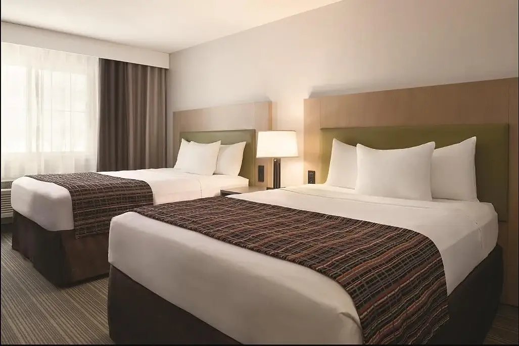 Two queen beds made up with white linen and a woven plaid runner